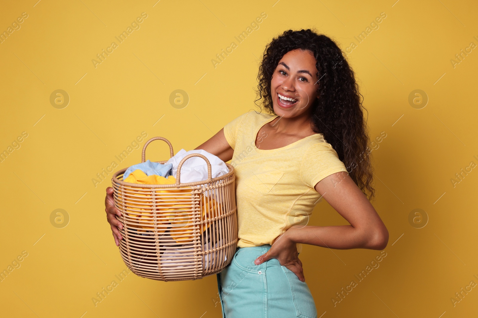 Photo of Happy woman with basket full of laundry on yellow background