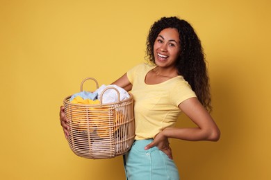 Photo of Happy woman with basket full of laundry on yellow background