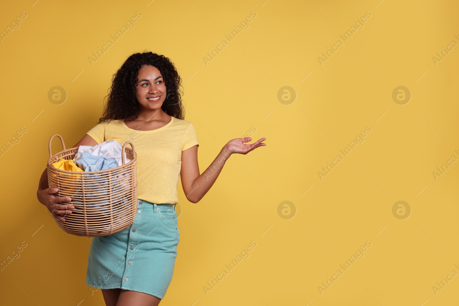 Photo of Happy woman with basket full of laundry on yellow background, space for text