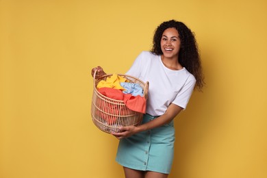 Photo of Happy woman with basket full of laundry on yellow background