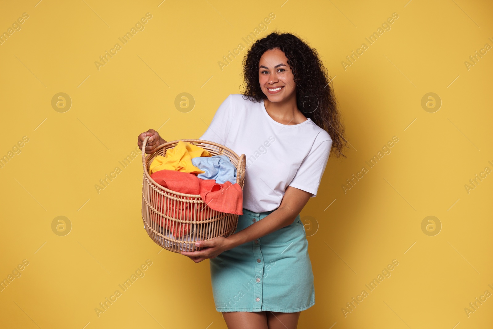 Photo of Happy woman with basket full of laundry on yellow background