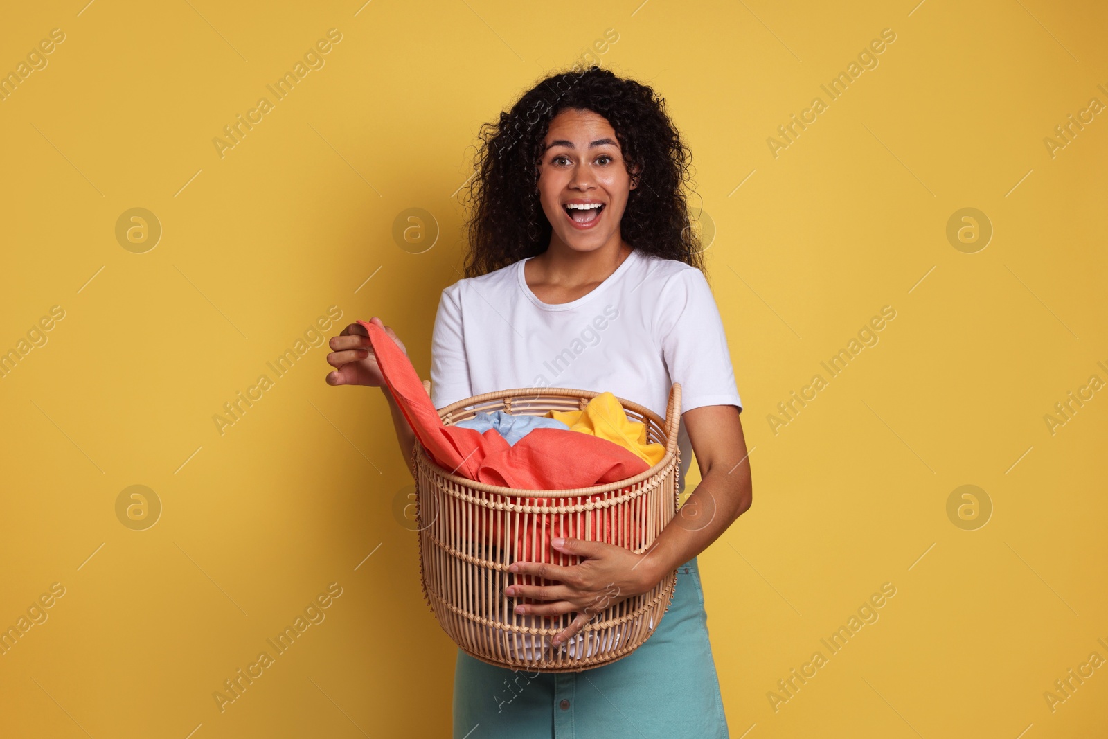 Photo of Happy woman with basket full of laundry on yellow background