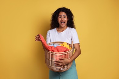 Happy woman with basket full of laundry on yellow background