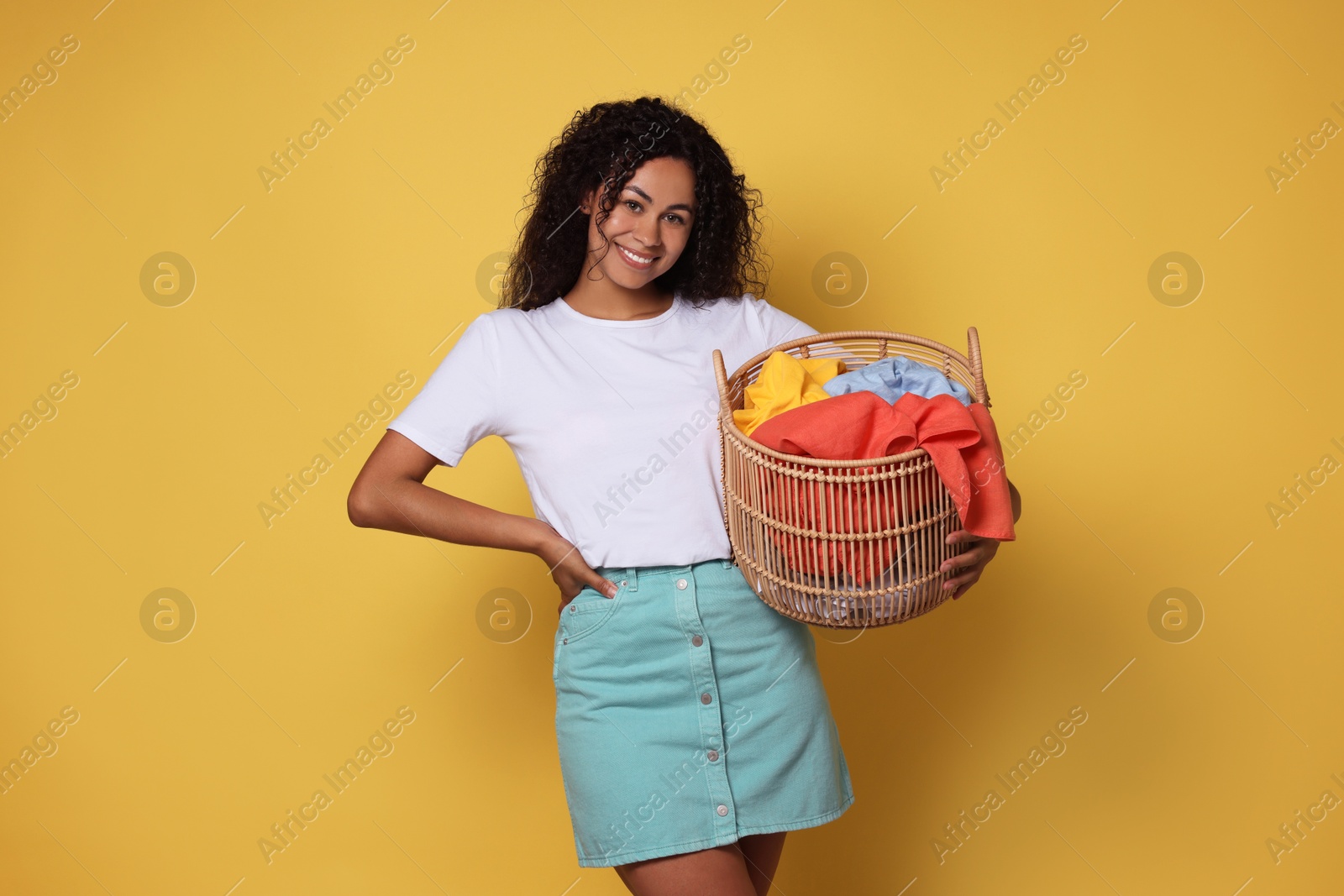 Photo of Happy woman with basket full of laundry on yellow background