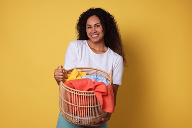 Photo of Happy woman with basket full of laundry on yellow background