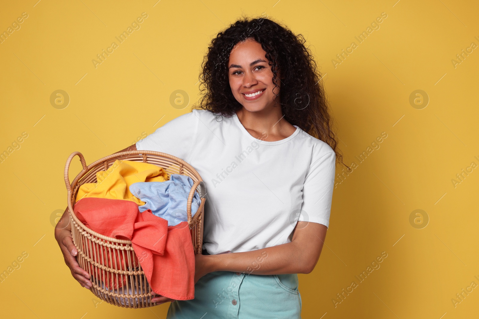 Photo of Happy woman with basket full of laundry on yellow background