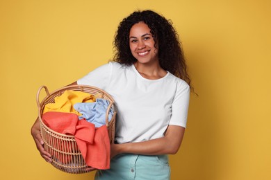 Photo of Happy woman with basket full of laundry on yellow background