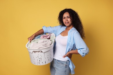 Photo of Displeased woman with basket full of laundry on yellow background