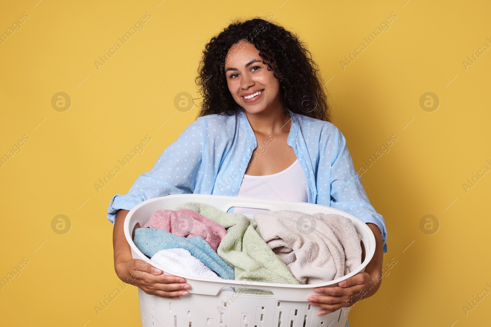 Photo of Happy woman with basket full of laundry on yellow background