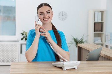 Professional receptionist talking on phone at wooden desk in hospital