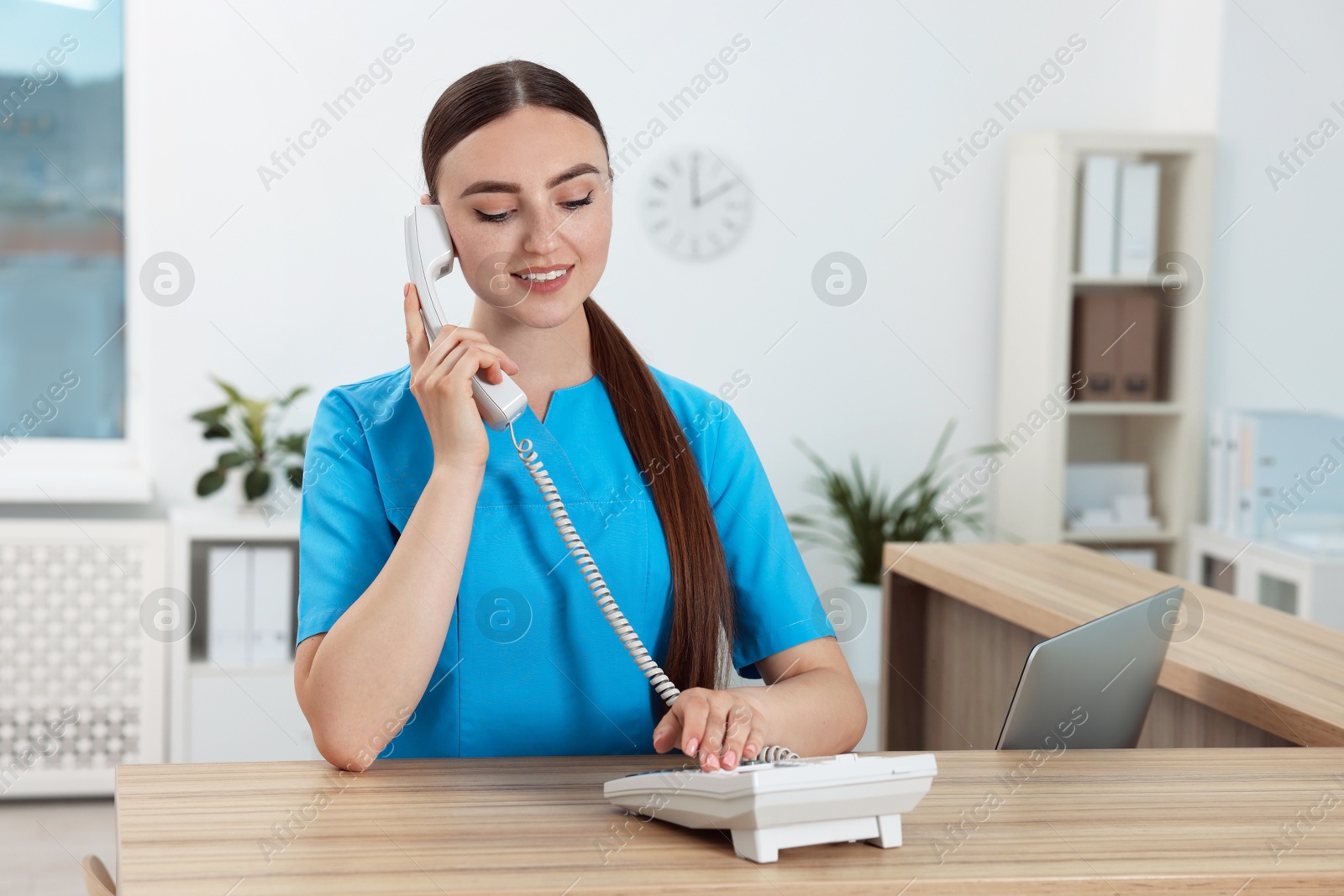 Photo of Professional receptionist talking on phone at wooden desk in hospital