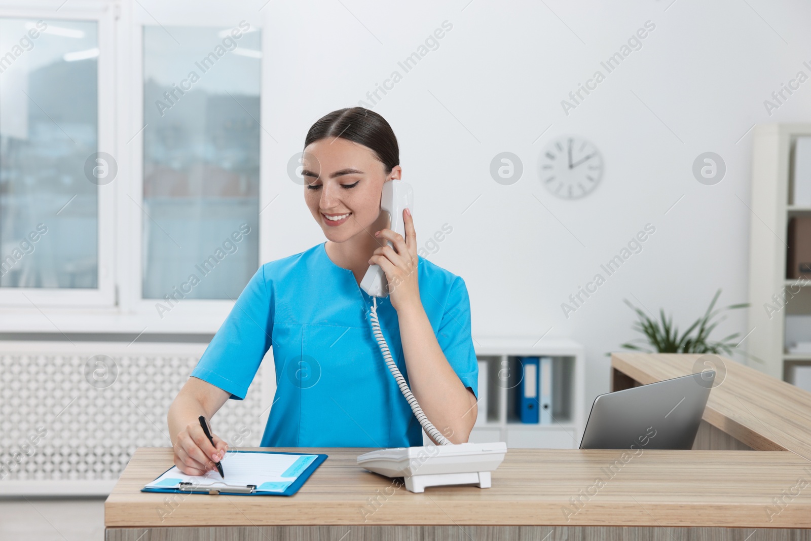 Photo of Professional receptionist talking on phone at wooden desk in hospital