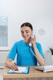 Professional receptionist talking on phone at wooden desk in hospital