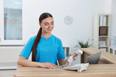 Photo of Professional receptionist talking on phone at wooden desk in hospital