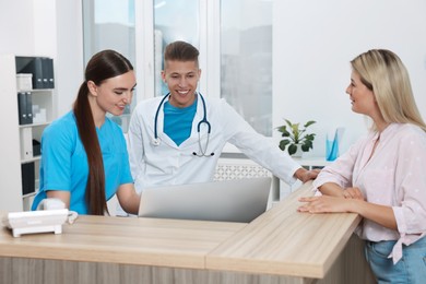 Photo of Professional receptionist and doctor working with patient at wooden desk in hospital