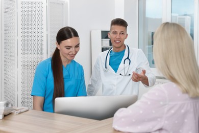 Photo of Professional receptionist and doctor working with patient at wooden desk in hospital