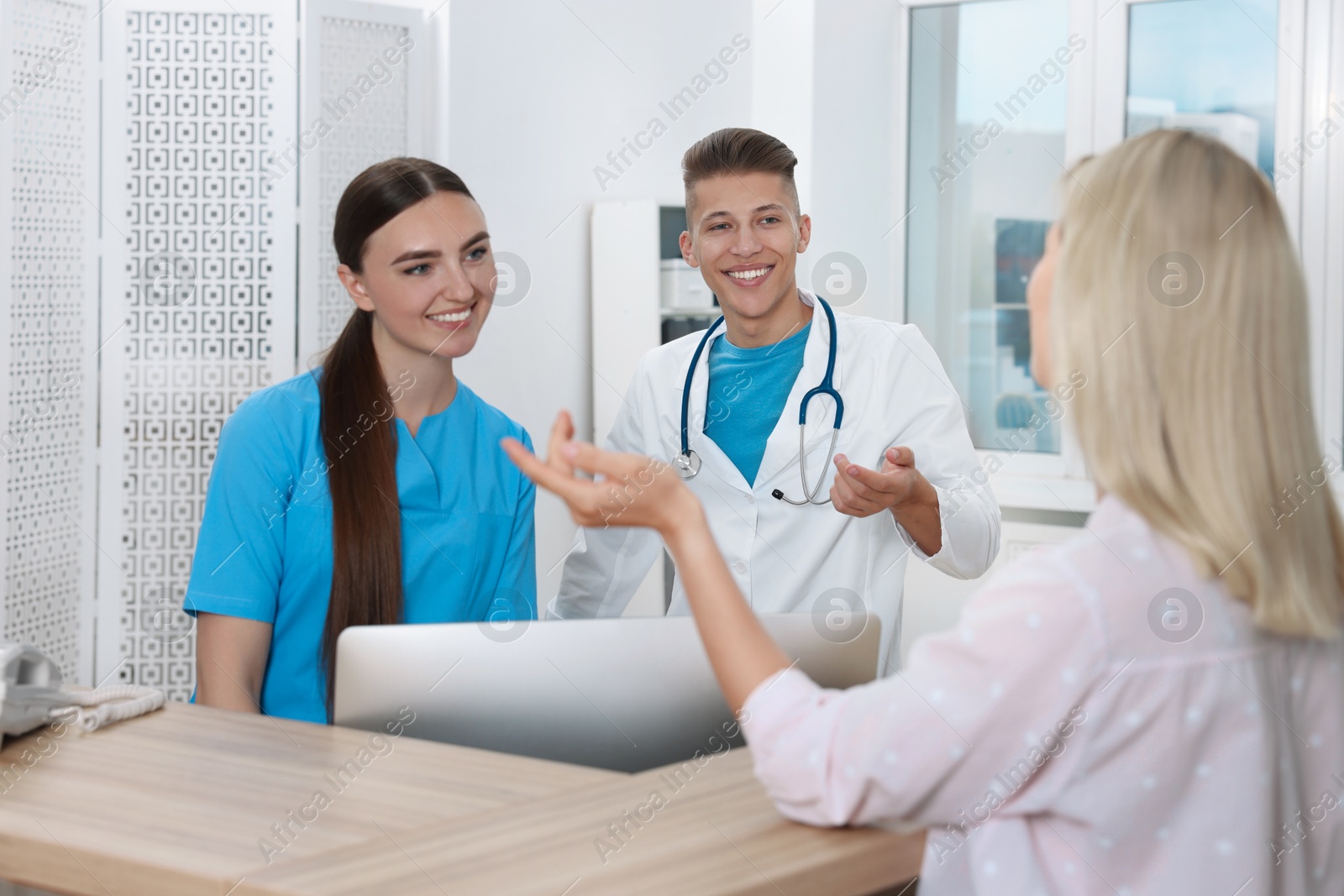 Photo of Professional receptionist and doctor working with patient at wooden desk in hospital