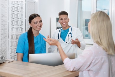 Professional receptionist and doctor working with patient at wooden desk in hospital