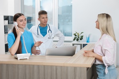 Photo of Professional receptionist and doctor working with patient at wooden desk in hospital