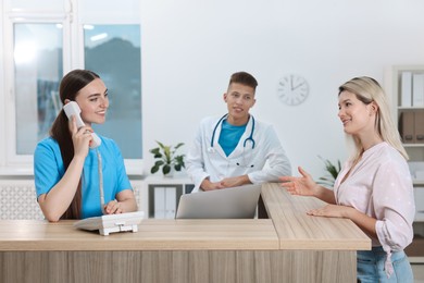 Photo of Professional receptionist and doctor working with patient at wooden desk in hospital