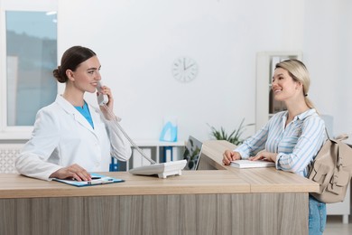 Professional receptionist working with patient at wooden desk in hospital