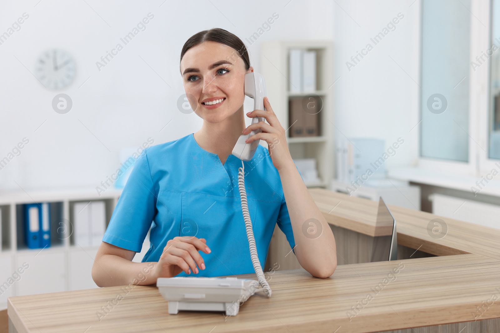 Photo of Professional receptionist talking on phone at wooden desk in hospital