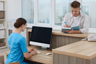 Professional receptionist working with patient at wooden desk in hospital