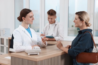 Photo of Professional receptionist working with patients at wooden desk in hospital