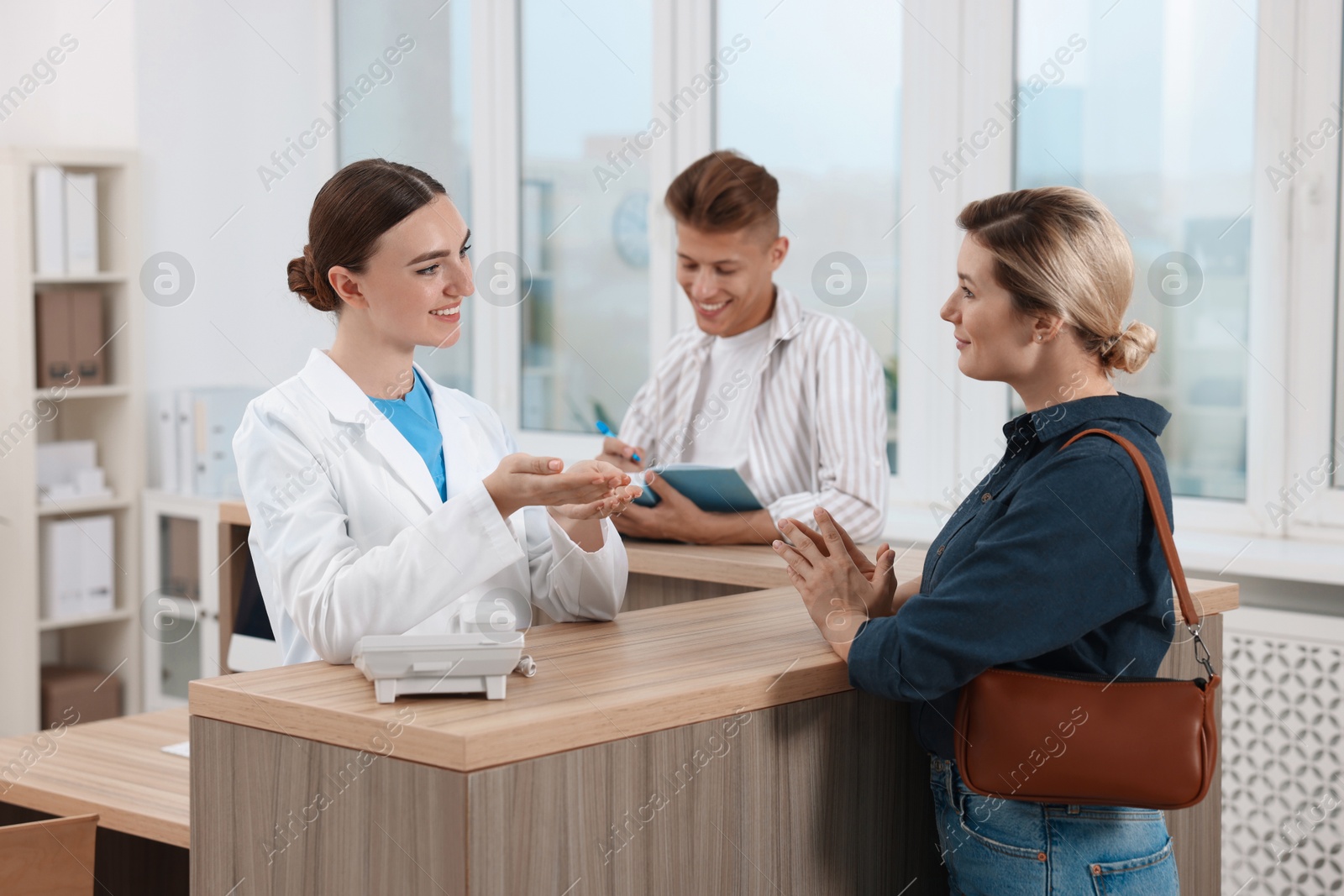 Photo of Professional receptionist working with patients at wooden desk in hospital