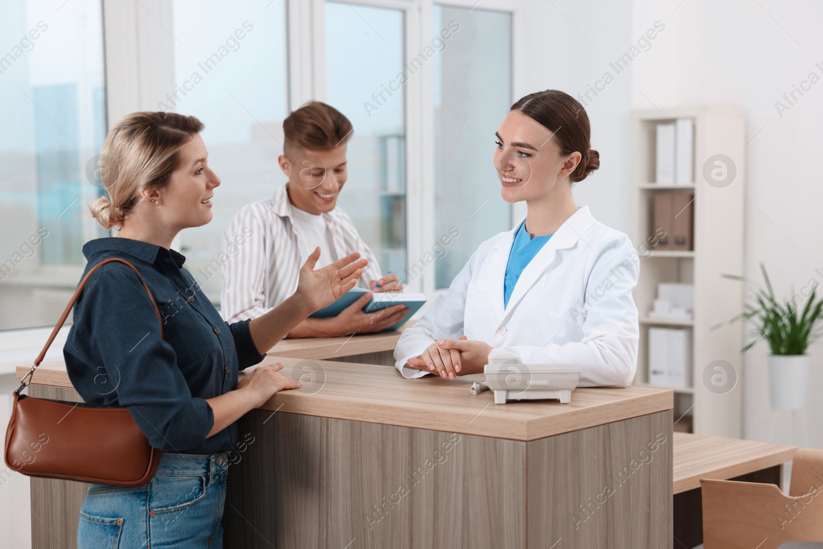 Photo of Professional receptionist working with patients at wooden desk in hospital