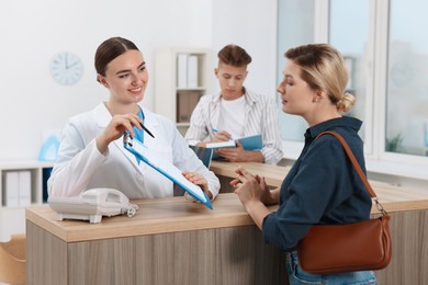 Professional receptionist working with patients at wooden desk in hospital