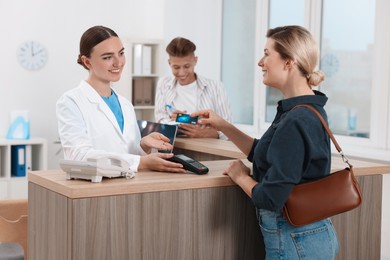 Receptionist taking payment from client via terminal at hospital