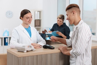 Receptionist taking payment from client via terminal at hospital