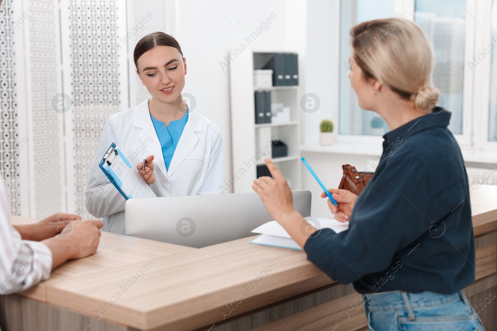 Photo of Professional receptionist working with patients at wooden desk in hospital