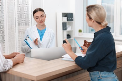 Professional receptionist working with patients at wooden desk in hospital