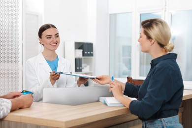 Professional receptionist working with patients at wooden desk in hospital