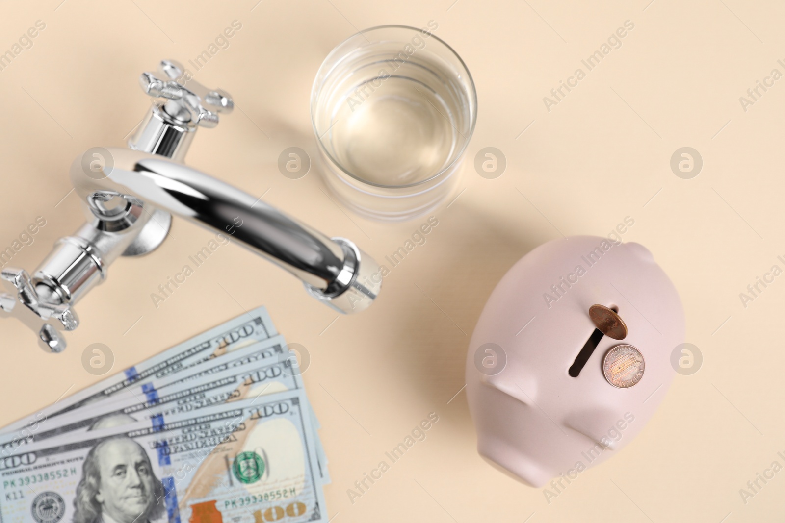 Photo of Water saving concept. Piggy bank, tap, glass of drink, dollar banknotes and coins on pale yellow background, flat lay