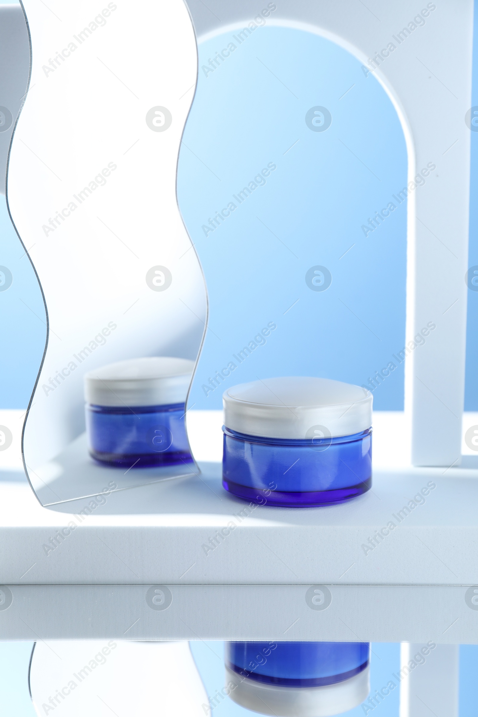 Photo of Stylish presentation of face cream in jar against light blue background