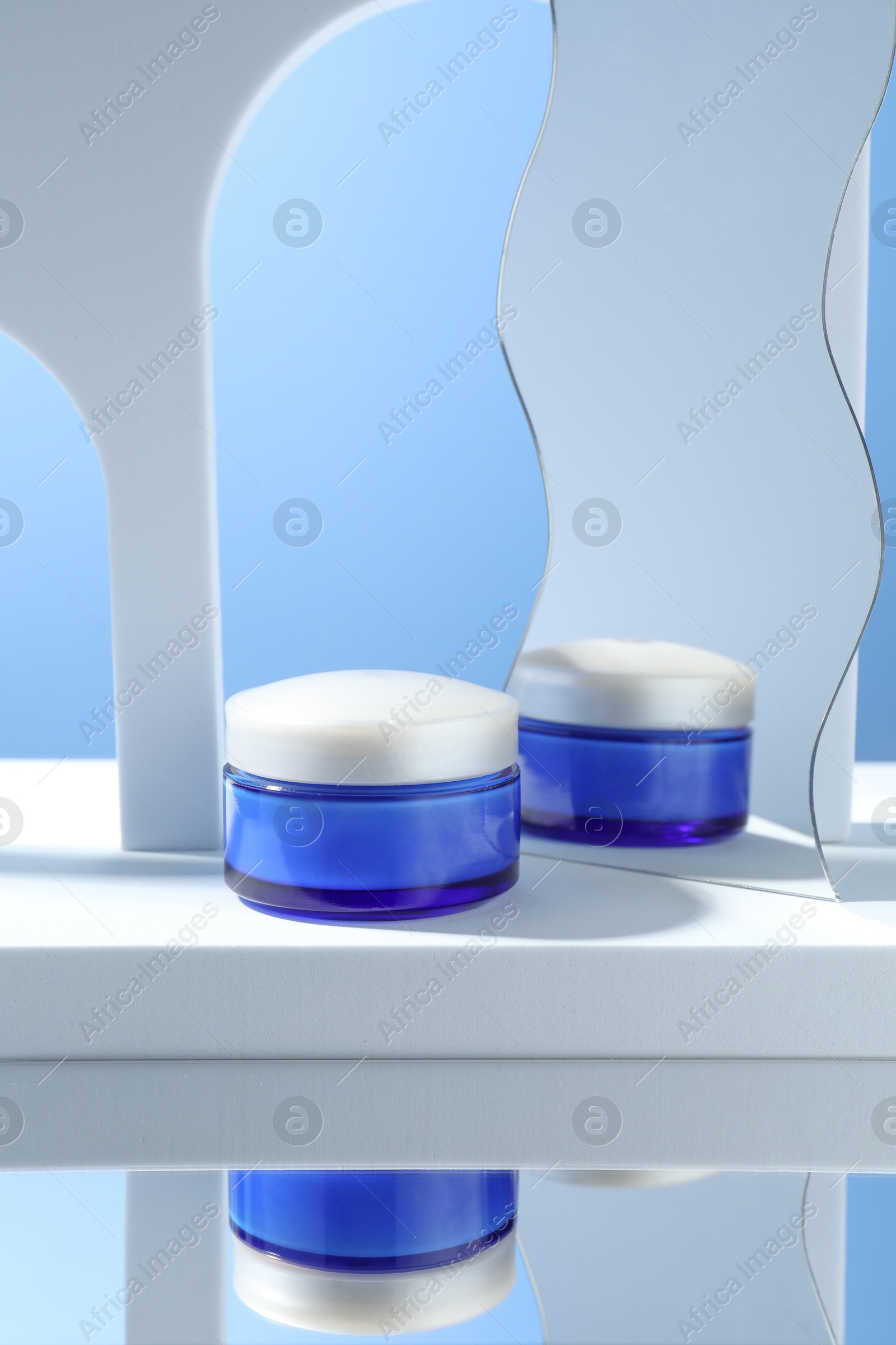 Photo of Stylish presentation of face cream in jar against light blue background