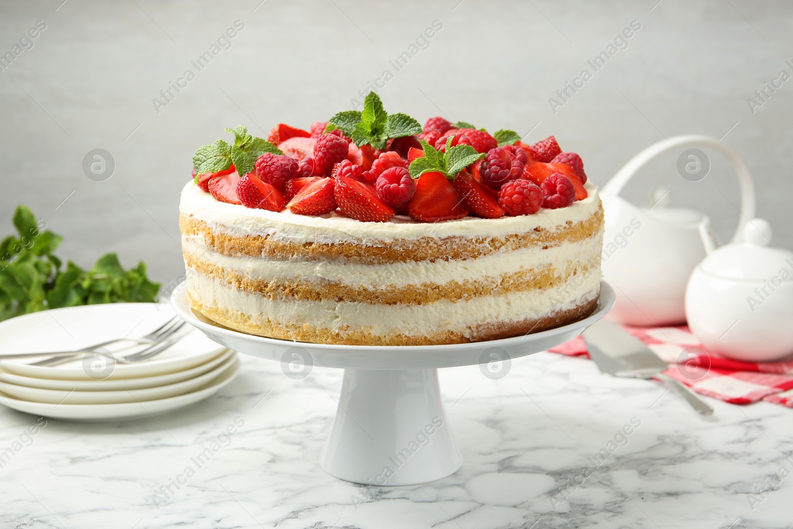 Photo of Tasty sponge cake with fresh berries and mint on white marble table