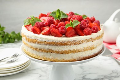 Tasty sponge cake with fresh berries and mint on white marble table, closeup