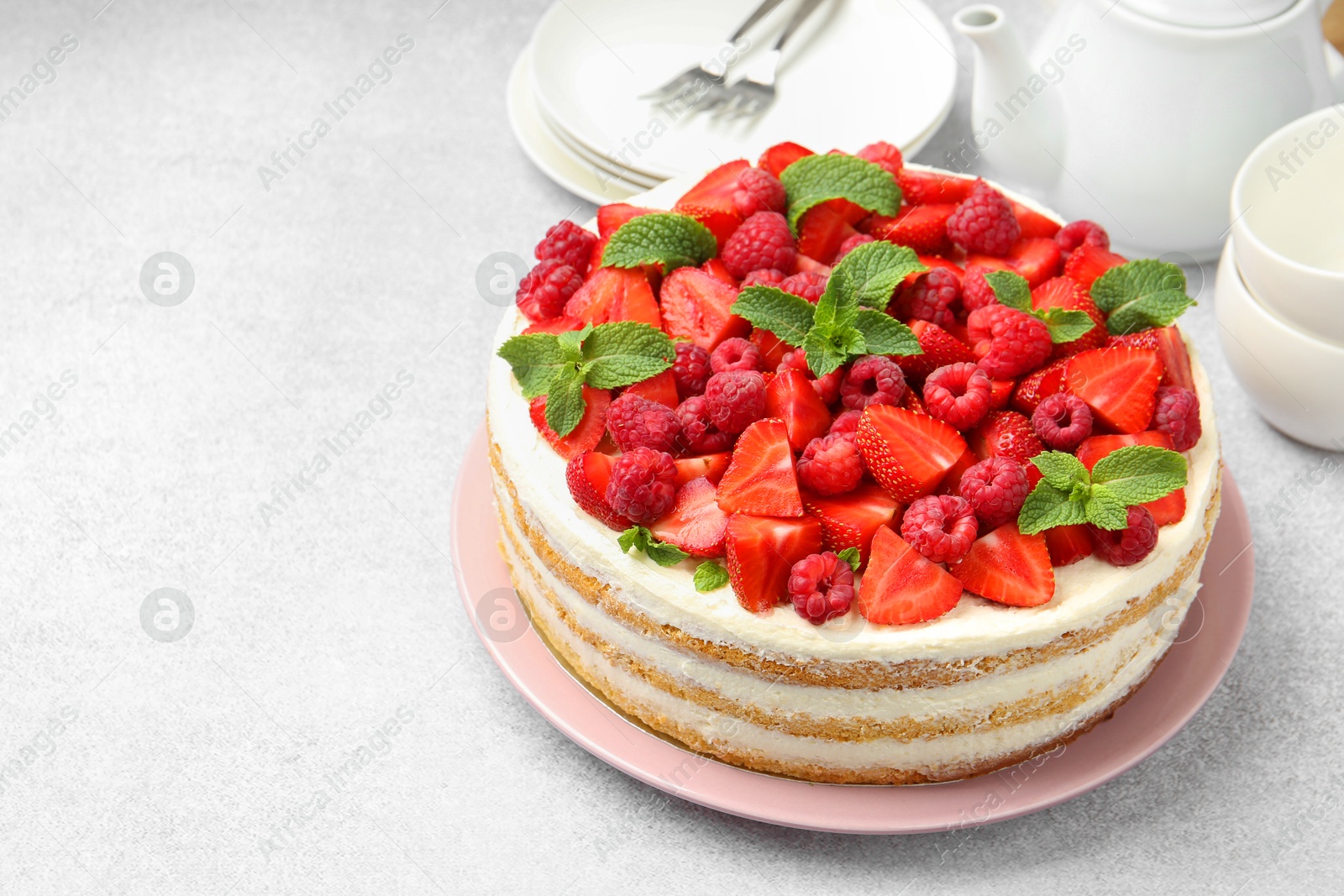 Photo of Tasty sponge cake with fresh berries and mint on light gray table, space for text