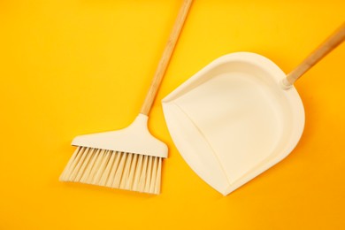 Photo of Cleaning broom and dustpan on orange background, flat lay