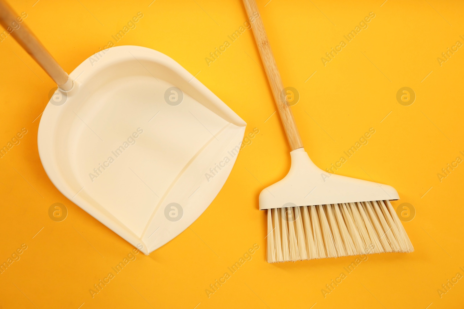 Photo of Cleaning broom and dustpan on orange background, flat lay