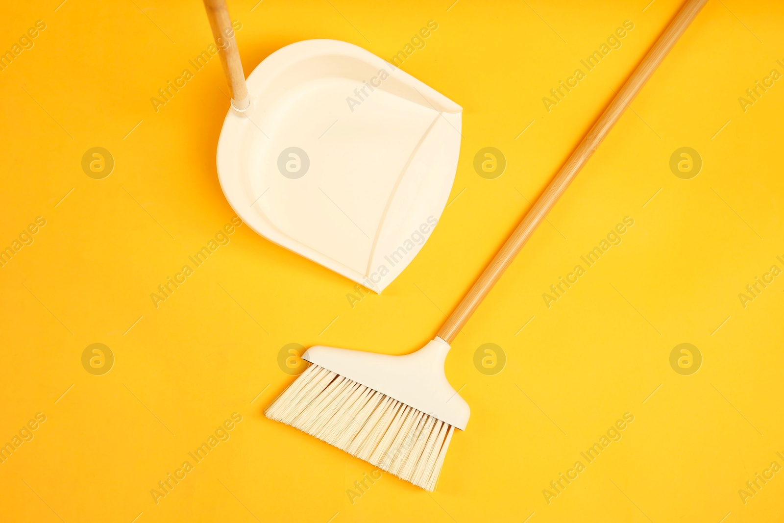 Photo of Cleaning broom and dustpan on orange background, flat lay