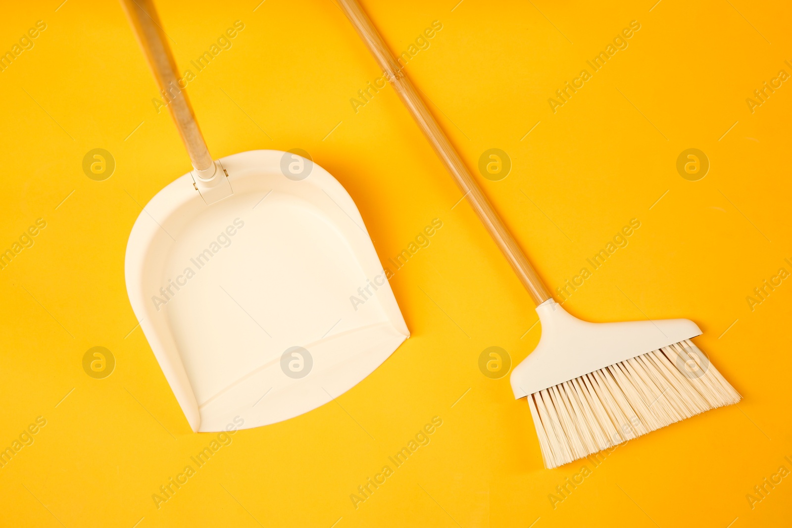 Photo of Cleaning broom and dustpan on orange background, flat lay