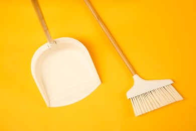 Photo of Cleaning broom and dustpan on orange background, flat lay