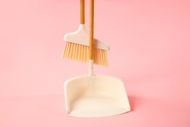 Cleaning broom and dustpan on pink background