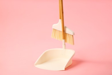 Photo of Cleaning broom and dustpan on pink background