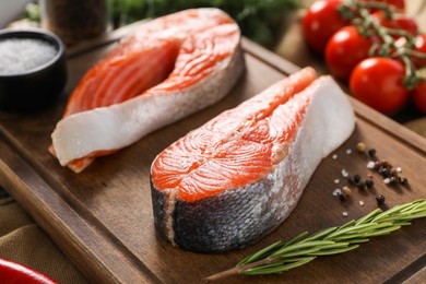 Board with fresh salmon steaks, rosemary and peppercorns on table, closeup